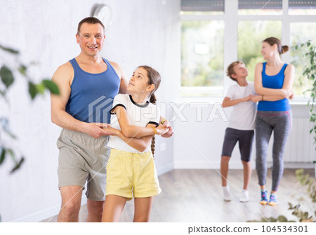 Positive preteen girl exercising dance moves with father during dance class, family practicing dance in pairs in studio Positive preteen girl exercising dance moves with father during dance class, family practicing dance in pairs in studio 104534301