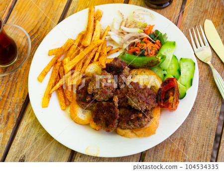 Spicy kofte (grilled minced meat) served with fresh cucumber, bread, vegetables and French fries on rustic wooden board Spicy kofte (grilled minced meat) served with fresh cucumber, bread, vegetables and French fries on rustic wooden board 104534335