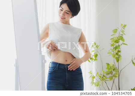 Woman checking her stomach in the mirror Woman checking her stomach in the mirror 104534705