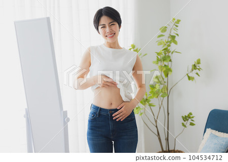 Woman checking her stomach in the mirror Woman checking her stomach in the mirror 104534712