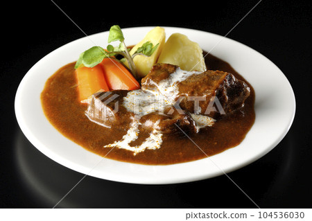 Watercress, carrot, potato garnish and fresh cream-covered thick-sliced beef tongue beef stew photographed against a black background 104536030