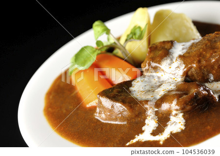 Watercress, carrot, potato garnish and fresh cream-covered thick-sliced beef tongue beef stew photographed against a black background 104536039
