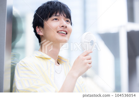 A young man cooling off with a portable fan A young man cooling off with a portable fan 104536054