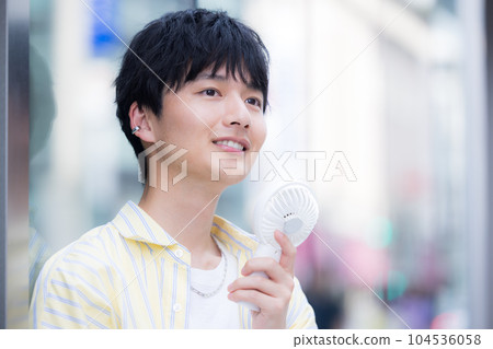 A young man cooling off with a portable fan 104536058