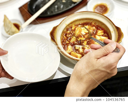 Hands separating mapo tofu into small plates 104536765