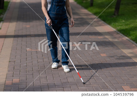 A faceless blind pregnant woman walks down the street with a cane.  104539796