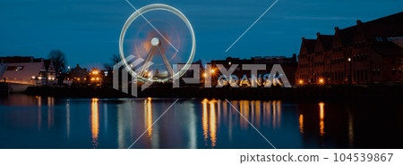 Gdansk Poland Ferris wheel in the old town of Gdansk at night evening dusk Reflection in river water Europe. Long exposure photo. City scenic view Illuminated attraction park and street Gdansk Poland Ferris wheel in the old town of Gdansk at night evening dusk Reflection in river water Europe. Long exposure photo. City scenic view Illuminated attraction park and street 104539867