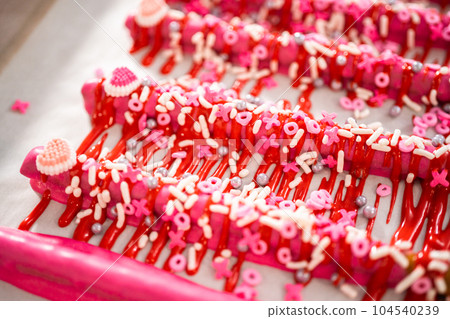 Drizzling melted chocolate over chocolate-dipped pretzels rods and decorating with sprinkles to make chocolate-covered pretzel rods for Valentine's Day. 104540239