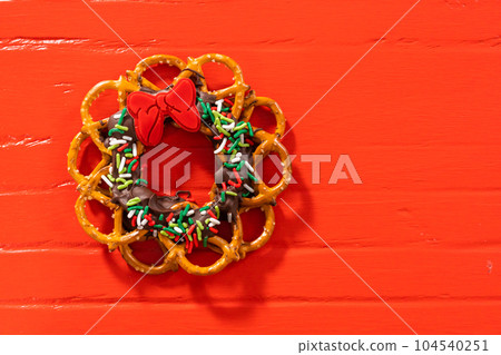 Chocolate pretzel Christmas wreath decorated with sprinkles and red chocolate bow on a red background. 104540251