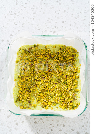 Freshly made homemade pistachio fudge in a square glass baking pan lined with parchment paper. 104540306