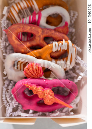 Packaging gourmet chocolate-covered pretzel twists into a white paper gift box filled with paper shreds. 104540308