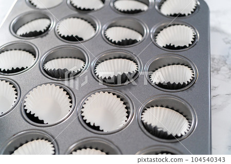 Scooping cupcake batter with dough scoop into a baking cupcake pan with liners to bake mini vanilla cupcakes with ombre pink buttercream frosting. 104540343