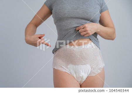 A cropped portrait of a woman pointing at adult diapers on her. Urinary incontinence problem. 104540344