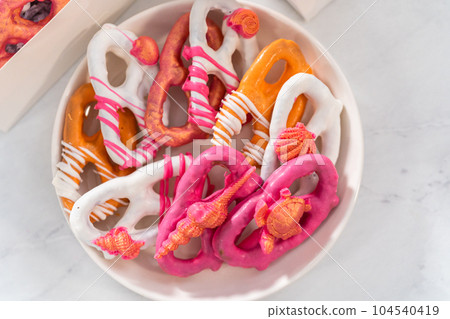 Packaging gourmet chocolate-covered pretzel twists into a white paper gift box filled with paper shreds. 104540419