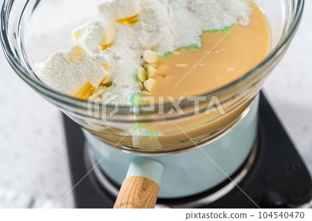 Melting chocolate chips and other ingredients in a glass mixing bowl over boiling water to prepare pistachio fudge. 104540470