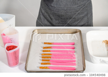 Dipping pretzels rods into silicone cup with melted chocolate to make chocolate-covered pretzel rods for Valentine's Day. 104540498