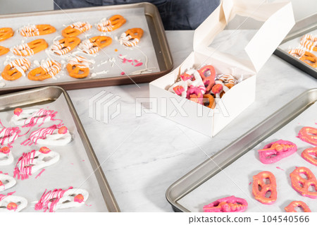 Packaging gourmet chocolate-covered pretzel twists into a white paper gift box filled with paper shreds. Packaging gourmet chocolate-covered pretzel twists into a white paper gift box filled with paper shreds. 104540566