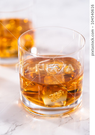 Scotch on the rocks in whiskey glass on a white marble surface. 104540616