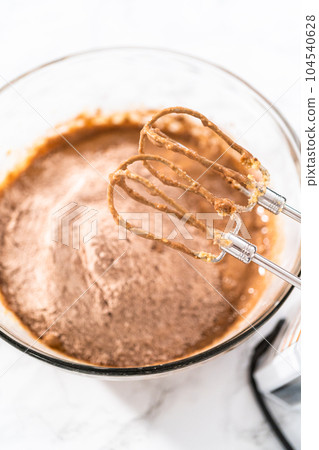 Mixing wet ingredients in a large glass mixing bowl to bake red velvet cupcakes with white chocolate ganache frosting. Mixing wet ingredients in a large glass mixing bowl to bake red velvet cupcakes with white chocolate ganache frosting. 104540628