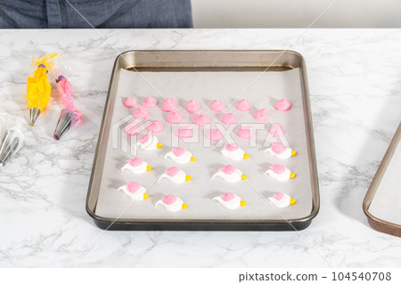 Piping meringue with piping bags into the baking sheet lined with parchment paper to bake Easter meringue cookies. 104540708