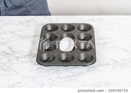 Lining cupcake pan with foil cupcake liners to bake red velvet cupcakes with white chocolate ganache frosting. Lining cupcake pan with foil cupcake liners to bake red velvet cupcakes with white chocolate ganache frosting. 104540734