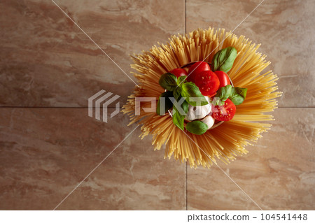 Raw spaghetti with tomato, garlic, and basil on a brown ceramic table. 104541448
