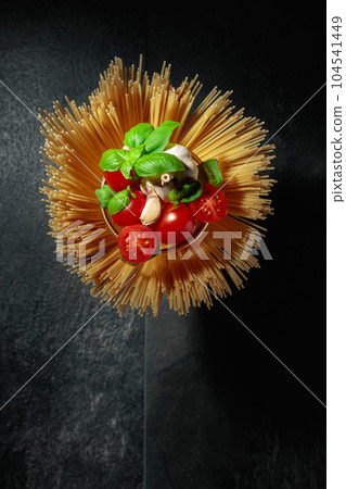 Raw spaghetti with tomato, garlic, and basil on a black stone table. Raw spaghetti with tomato, garlic, and basil on a black stone table. 104541449