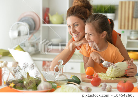 Portrait of girl with her mother cooking together at kitchen table 104542603