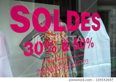 closeup of discount sign "SOLDES jusqu'a 30%, 50%" in french,  the traduction of  (sales until 30% , 50%) on window in french fashion store showroom on summer clothes background 104542697