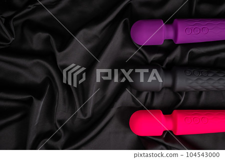 Three colored dildos on a black silk sheet.  104543000