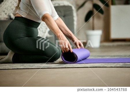 Senior woman in leggings and t-shirt preparing for training at home, putting in fitness matt. Keeping body in tone Senior woman in leggings and t-shirt preparing for training at home, putting in fitness matt. Keeping body in tone 104543788