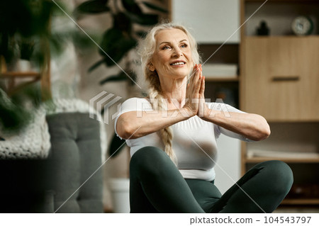 Beautiful, positive, senior woman sitting on fitness matt in living room, training, doing yoga exercises at home. Meditation Beautiful, positive, senior woman sitting on fitness matt in living room, training, doing yoga exercises at home. Meditation 104543797