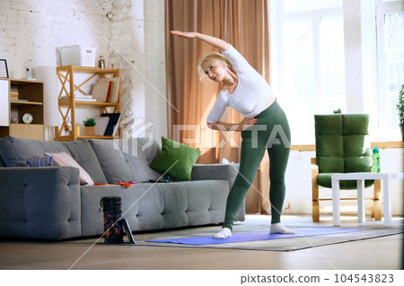 Senior beautiful woman in comfortable sportswear training at home, doing warming-up and stretching exercises 104543823