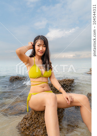 Sexy asian woman Wear a yellow body suit. Sitting on a rock in the sea Sexy asian woman Wear a yellow body suit. Sitting on a rock in the sea 104544311