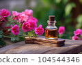 Fragrant Rose Geranium Essential Oil in small transparent glass Bottle on a wooden surface next to fresh Pink Geranium Flowers in full bloom, Garden background with Copy space. 104544346
