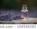 Fragrant Lavender Essential Oil in small transparent glass Bottle on a wooden surface next to fresh Lavandula Flowers, field background. 104544383