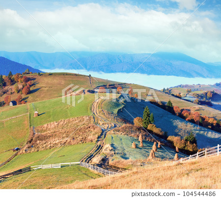 Autumn misty morning plateau with stack of hay and country dirty road (Mighgirya village outskirts, Carpathian Mountains, Ukraine). 104544486