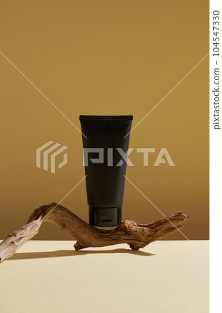 Minimalist abstract background for cosmetics or products presentation. A black plastic tube unbranded placed on dry twig on brown background. Front view, space for design Minimalist abstract background for cosmetics or products presentation. A black plastic tube unbranded placed on dry twig on brown background. Front view, space for design 104547330