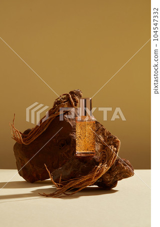 Front view of serum bottle unlabeled displayed on brown stone with angelica sinensis roots on brown background. Minimal scene with copy space for business branding and product presentation. Front view of serum bottle unlabeled displayed on brown stone with angelica sinensis roots on brown background. Minimal scene with copy space for business branding and product presentation. 104547332