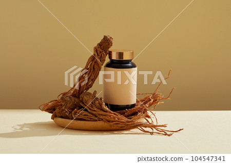 Front view of medicine bottle unbranded placed on wooden dish with angelica sinensis root (Dang Gui) on brown background. Mockup for advertising, empty space for design packaging.  104547341