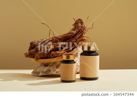 Angelica sinensis root placed on wooden dish on stone and two bottle unbranded container medicine decorated on brown background. Mockup for product with herbal. Front view 104547344