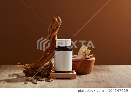 Bai Zhu are contained inside a wooden bowl, arranged with Angelica root and many pills. Blank label glass jar standing on a small podium Bai Zhu are contained inside a wooden bowl, arranged with Angelica root and many pills. Blank label glass jar standing on a small podium 104547469