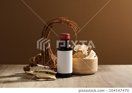 Empty label glass bottle placed on table with Angelica root and a wooden bowl of Bai Zhu. These herbs that are often used in traditional medicine 104547470