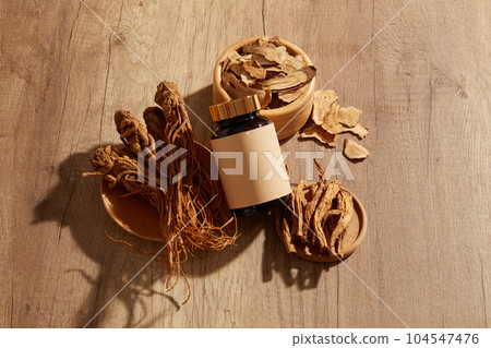 Angelica root placed on wooden plates and a wooden bowl of Bai Zhu arranged with an unlabeled glass jar of medicine. Mockup of traditional medicine branding Angelica root placed on wooden plates and a wooden bowl of Bai Zhu arranged with an unlabeled glass jar of medicine. Mockup of traditional medicine branding 104547476