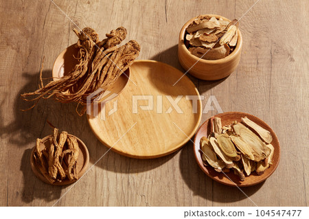 A wooden plate in round-shaped with several plates of Bai Zhu and Angelica root displayed around. Blank space for medicine product presentation 104547477