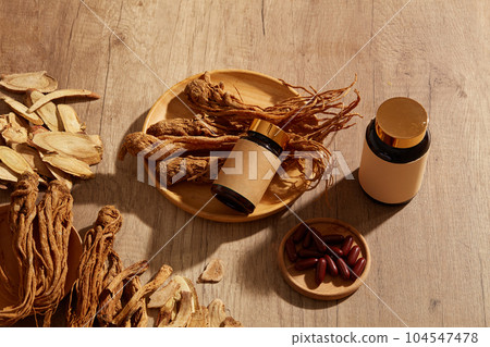 Small dish of red pills arranged with Angelica root and Bai Zhu. Traditional medicine bottles without label are displayed. For medicine advertising 104547478