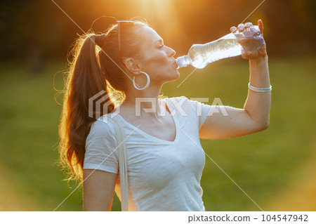 smiling modern woman in white shirt drinking water 104547942