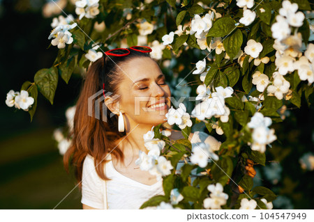 smiling trendy woman in white shirt near flowering tree smiling trendy woman in white shirt near flowering tree 104547949