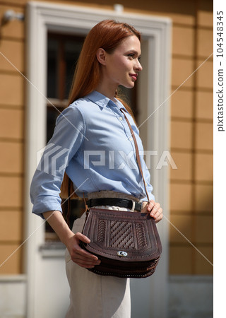 woman posing with a small brown leather bag with a carved pattern. 104548345