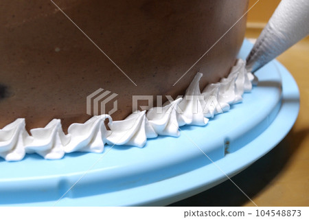 A woman pastry chef with a pastry bag in her hands squeezes cream on a cake in a home kitchen. Professional chef at work on bakery kitchen. culinary, baking and cooking food concept, home cooking 104548873